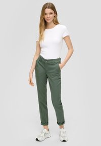 Groene katoenen broek met een getailleerde pasvorm, rechte pijpen en omgeslagen pijpen. Gepaard met een witte top met korte mouwen en witte sneakers.