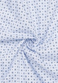 Tessuto azzurro chiaro con un motivo geometrico ripetuto di piccoli cerchi e diamanti in tonalità di blu più scure, caratterizzato da una superficie texturizzata.