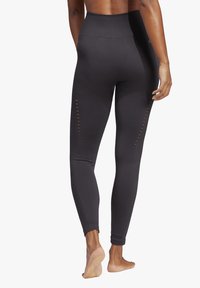 Leggings neri a vita alta con una texture liscia, caratterizzati da dettagli a fessura verticale lungo i lati esterni e polsini aderenti alla caviglia.