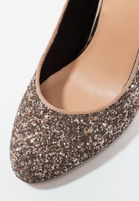 Chaussure plate à bout pointu recouverte de paillettes avec une bordure beige et une semelle intérieure lisse couleur sable.