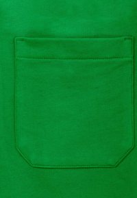 Tessuto verde con una texture liscia, caratterizzato da una tasca rettangolare con dettagli di cucitura in alto, centrata sul capo.