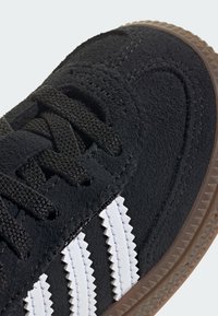 Sorte semskede sneakers med teksturert overflate, med hvite taggete tre striper, sorte snører og gummisåle.