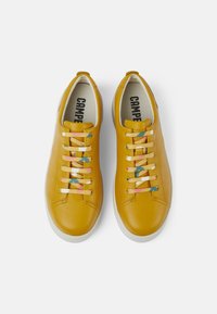 Žluté kožené tenisky s hladkým povrchem, vybavené vícebarevnými tkaničkami. Sólové části jsou bílé a mají minimalistický design.