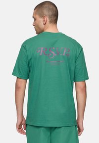Groene katoenen t-shirt met paarse tekst "R.S.V.P." en "fila tennis society" op de rug. Korte mouwen en een relaxte pasvorm.