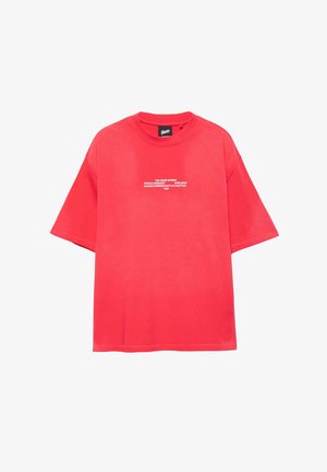 Rdeča bombažna majica s kratkimi rokavi in sproščenim krojem. Spredaj ima belo besedilo. Enostaven kroj z okroglim izrezom brez dodatnih poudarkov.