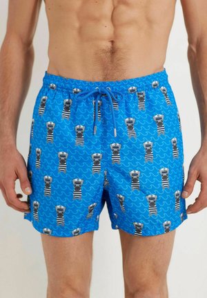 Pantaloni scurți de înot albaștri cu un model jucăuș de urși cartoon îmbrăcați în costume de marinar, cu talie cu șnur și buzunare laterale. Textură de țesătură netedă.