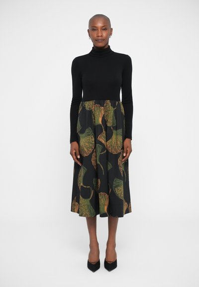 Top negro de cuello alto combinado con una falda midi de patrón floral en negro, verde y naranja. Presenta un diseño acampanado y una textura suave.