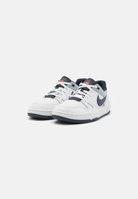 Sneaker basse bianche con accenti blu navy. Parte superiore in pelle liscia, colletto imbottito, chiusura con lacci e suola in gomma testurizzata. Logo Nike sul lato.