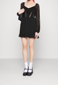 Black dress with sheer, puffed sleeves, textured dot pattern, ruffled hem, and lace detailing. Paired with black platform shoes and white socks.