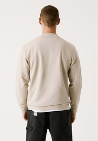 Sudadera de manga larga beige con cuello redondo, textura suave y puños acanalados. Combinada con pantalones cargo oscuros con bolsillos.
