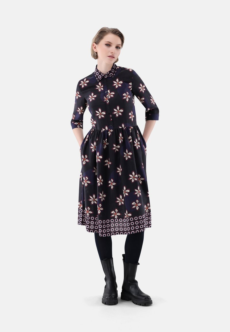 Blumenmuster, knopfbehangenes Kleid in Marineblau mit Dreiviertelärmeln, tailliertem Schnitt und Taschen. Vollendet mit einem kontrastierenden gemusterten Saum.