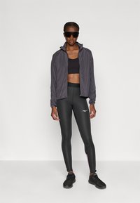 Sort atletisk crop top, let grå jakke og sorte tights med lyserøde detaljer. Iført mørke solbriller og sorte sneakers.