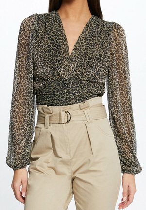 Blusa transparente de manga larga con estampado de leopardo, metida dentro de pantalones beige de talle alto con un cinturón de tela a juego y hebilla de doble anillo.