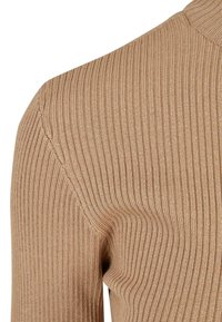 Beige ribbe sweater som har høy hals, teksturert stoff og en tettsittende design. Materialet ser mykt og elastisk ut.