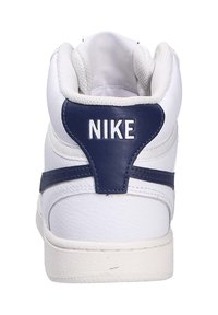 Sneaker in pelle bianca con design high-top, caratterizzata da una linguetta sul tallone e lacci blu navy, e un logo Nike bianco sul retro.