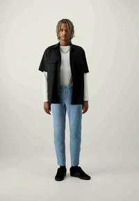 Black short-sleeve shirt, white long-sleeve shirt underneath, light blue slim-fit pants, wearing black sneakers, standing against a neutral background.