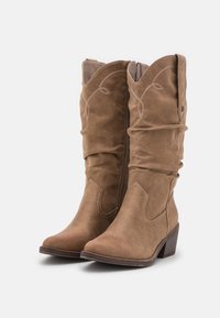 Botas de vaquero de ante marrón con un diseño arrugado, punta afilada y costuras decorativas. Cuenta con un tacón bajo apilado y cremallera lateral.