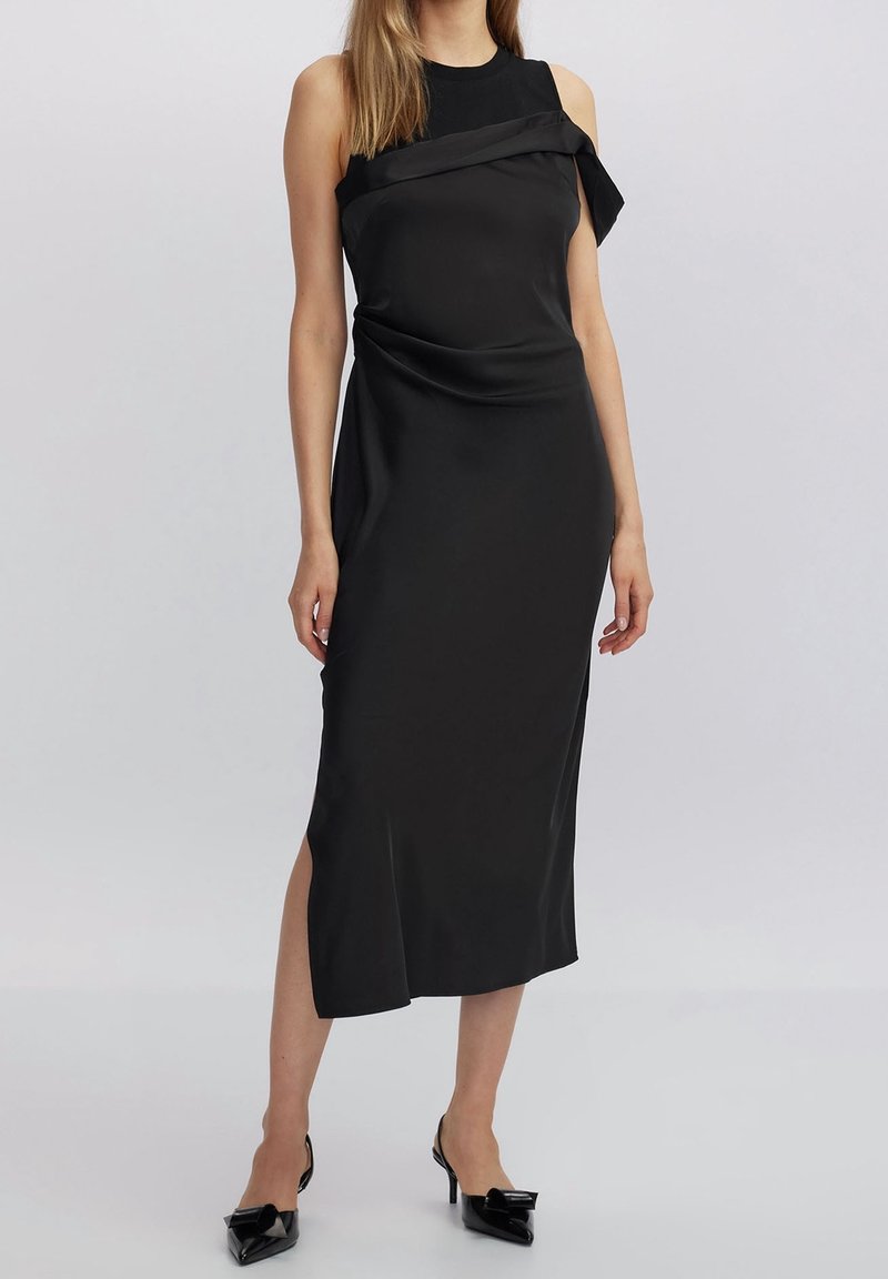 Musta hihaton mekko, jossa on laskostettu muotoilu, sivureikä ja sileä tekstuuri. Yhdistetty kärkitossuihin, joissa on nauhaaccentti.