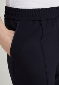 Marina blå byxor med en mjuk textur, med en rynkad midja och sidfickor, framhävd av kontrasterande kant längs fickkanten.