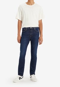 Mörkblå denimjeans med rak passform, kombinerade med en vit bomullströja. Skorna består av vita sneakers med svarta detaljer.