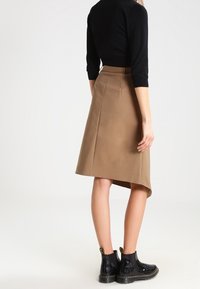 Brun asymmetrisk kjol i mjukt tyg, kombinerad med en åtsittande svart topp och blanka svarta ankelstövlar med subtila detaljer.