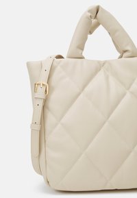 Sac à main en cuir matelassé crème avec poignée supérieure rembourrée et bandoulière réglable avec boucle dorée.