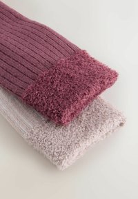 To sæt strikkede benvarmere: et i mørke lilla ribstrik med en blød, fuzzy manchet, og et andet i lys pink med en glat tekstur.