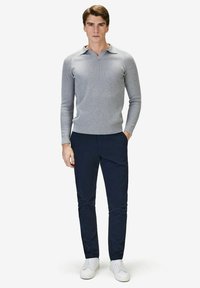 Ljusgrå ribbad stickad tröja med krage, kombinerad med marinblå chinos och vita sneakers, vilket skapar en avslappnad outfit.