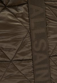 Prošívaná hnědá nylonová tkanina má texturovaný doplňkový popruh s vyraženým písmem. Povrch má jemný lesk a geometrický vzor.