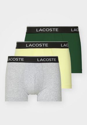 Tres pares de boxers para hombre: gris, amarillo y verde. Cada uno con una cinturilla negra que presenta el texto "LACOSTE" en blanco.