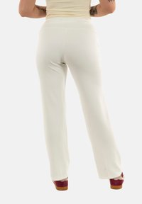 Pantalones de tiro alto en beige claro con una tela suave y elástica, de piernas anchas y con detalles de costura mínimos, combinados con zapatos de plataforma burdeos.