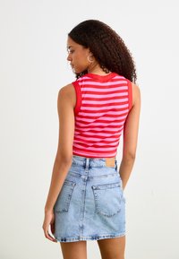 Top corto senza maniche a righe rosse e rosa con texture a coste, abbinato a una mini gonna di denim azzurro chiaro, con tasche posteriori e etichetta.