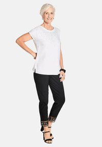 Witte top met korte mouwen en details van rhinestones, gecombineerd met zwarte broek met uitgebreide borduursels op de manchetten en zwarte gespsandalen.