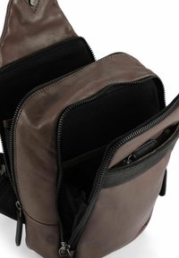 Bruine leren rugzak met textuur, voorzien van twee ritssluitingen en een voorvak met een gladde afwerking en zwarte accenten.