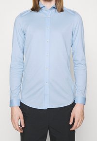 Camicia azzurro chiaro a maniche lunghe in cotone, con colletto button-down, patta frontale con bottoni e design aderente.