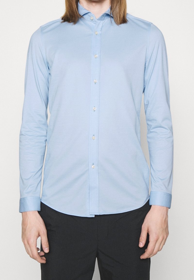 Camicia azzurro chiaro a maniche lunghe in cotone, con colletto button-down, patta frontale con bottoni e design aderente.