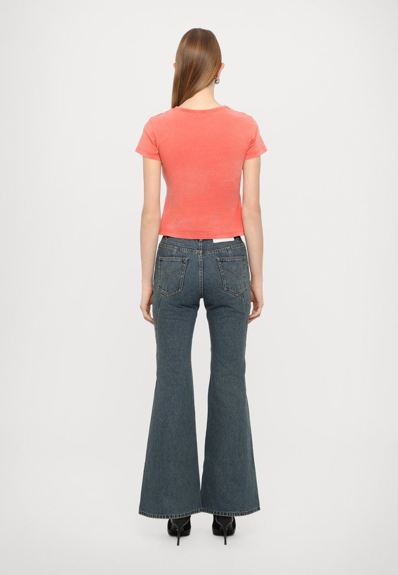 Camiseta de manga corta color coral combinada con jeans acampanados de cintura alta en azul oscuro, con bolsillos traseros y dobladillo sin rematar. Zapatos de tacón negros.