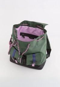 Mochila impermeable verde con acentos rosas, cordón ajustable, dobles bolsillos exteriores y una base negra contrastante. Forrada en púrpura claro.