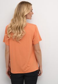 Short-sleeve t-shirt in coral, soft material, relaxed fit, with a rounded neckline and smooth texture. Back view shows a simple design.
