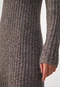 Robe en tricot côtelé gris avec des manches longues et une silhouette ajustée ornée d'un motif texturé. Gros plan sur le tissu et le détail des mains.