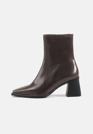 Bottine en cuir marron avec un bout pointu et un talon épais noir. Texture lisse, design minimaliste et sans ornement visible.
