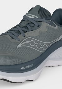 Γκρι αθλητικό παπούτσι Saucony με πάνω μέρος από δίχτυ, κλείσιμο με κορδόνια, λευκή σόλα και κείμενο ""incrediLUX"" στη μεσόσολα.