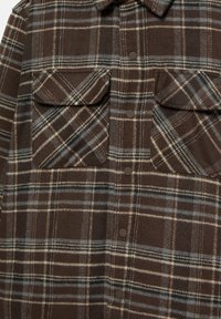 Camicia a quadri marrone realizzata in tessuto morbido, con due tasche sul petto, bottoni automatici e linee contrastanti blu e crema nel motivo.