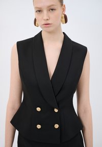 Schwarze ärmellose Blazer mit tiefem V-Ausschnitt, ausgestattet mit einem doppelt geknöpften Design und goldenen Knotenknöpfen, taillierte Passform, glatte Textur.