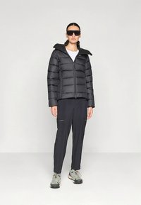 Svart boblejakke med høyt krage, glidelås og horisontale sømmer; kombinert med mørke bukser og lyse treningssko.