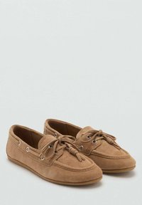 Ein Paar beige Wildleder-Mokassinschuhe mit Schnürdetails und Metallösen, nebeneinander auf einer hellen Oberfläche platziert.