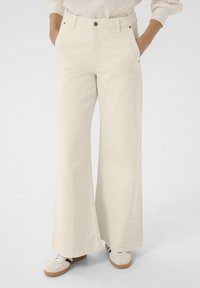 Pantalon beige à jambes larges en coton doux, avec poches avant, fermeture par bouton, et une texture lisse et épurée.
