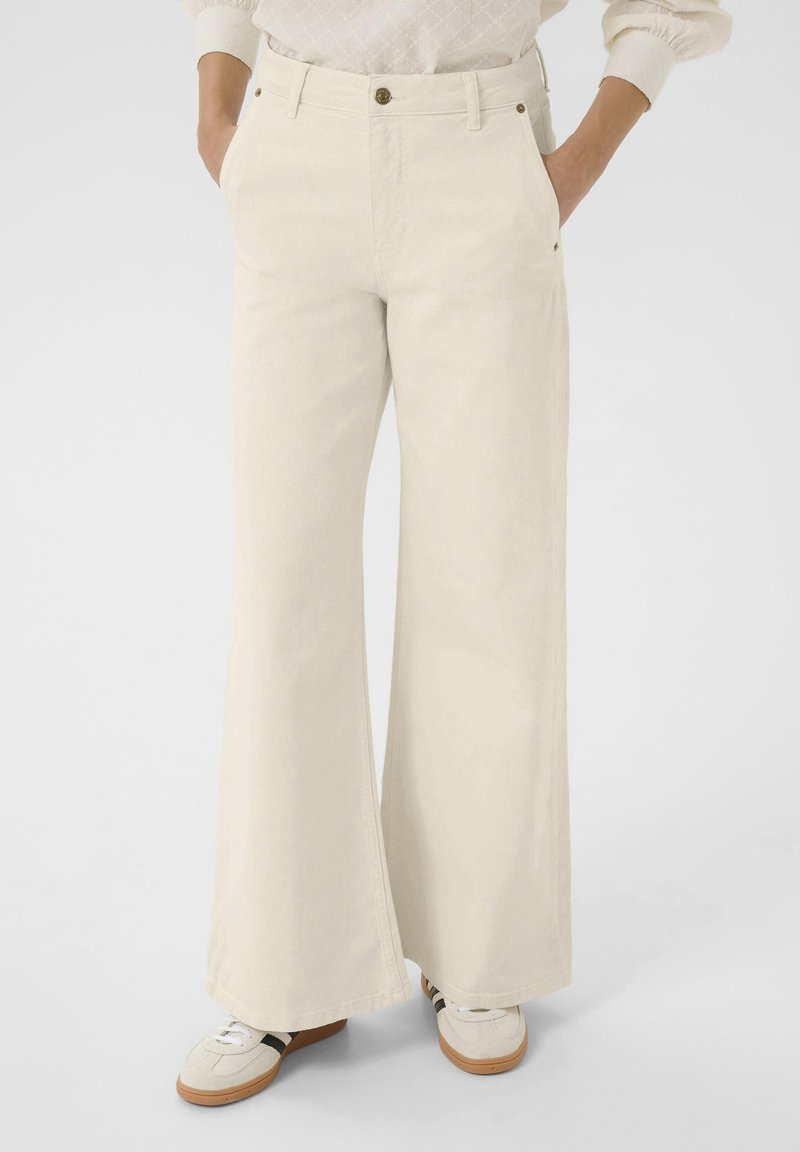 Pantalon beige à jambes larges en coton doux, avec poches avant, fermeture par bouton, et une texture lisse et épurée.