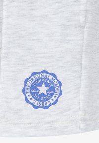 Szary t-shirt z materiału, z okrągłym niebieskim logo i białym napisem "The Original" oraz "Converse All Star 1908" wkomponowanym w wzór gwiazdy.