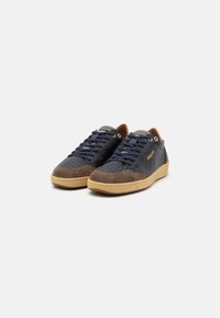 Sneaker blu navy e marrone in suede e pelle liscia, con area delle dita perforata, lacci blu navy, dettagli marroni e suola in gomma beige.